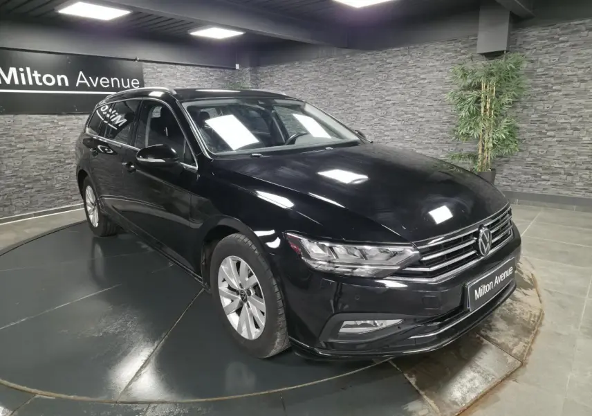 Volkswagen Passat SW noire vue 3/4 avant droit en intérieur avec calandre chromée et jantes alliage 16 pouces.