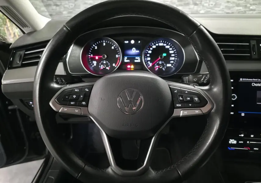 Vue rapprochée du volant cuir noir multifonction d'une Volkswagen Passat 2024 avec tableau de bord et écran tactile visibles.