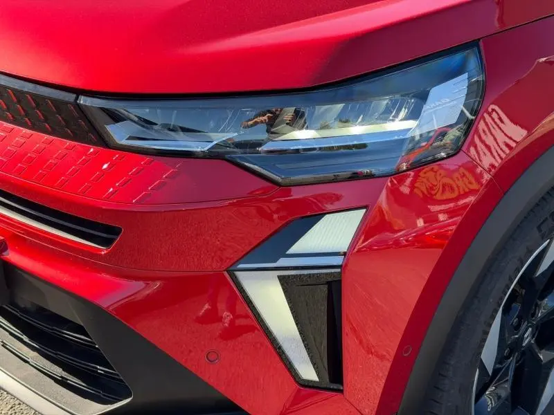 Gros plan sur l'avant droit du Renault Captur 2025 Rouge Flamme, mettant en valeur le phare et la calandre moderne.