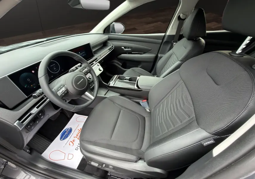 Vue intérieure côté conducteur du Hyundai Tucson 1.6 Hybrid 239 Creative 2026, sièges noirs et tableau de bord digital.