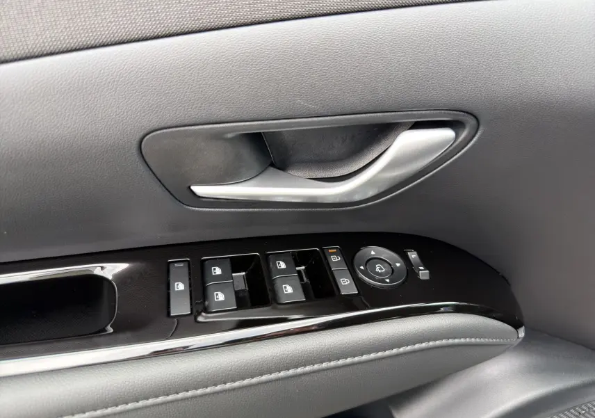 Poignée de porte intérieure côté conducteur avec commandes électriques des vitres et rétroviseurs sur Hyundai Tucson gris foncé 2026.