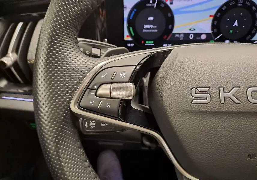 Gros plan sur le volant perforé gris perle du Skoda Kodiaq 2025, avec commandes multifonctions et tableau de bord numérique en arrière-plan.