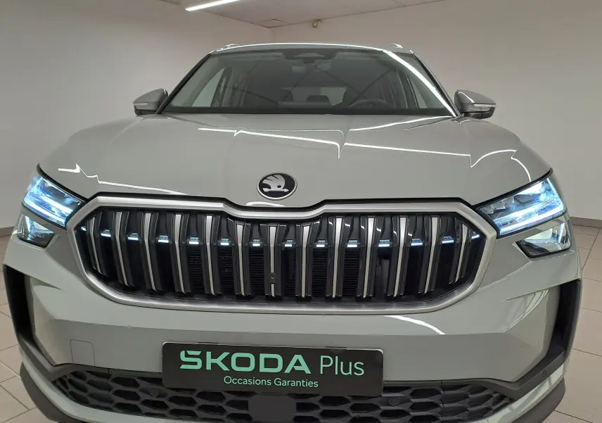 Vue frontale d'un Skoda Kodiaq gris perle avec calandre verticale et phares LED allumés en intérieur showroom.