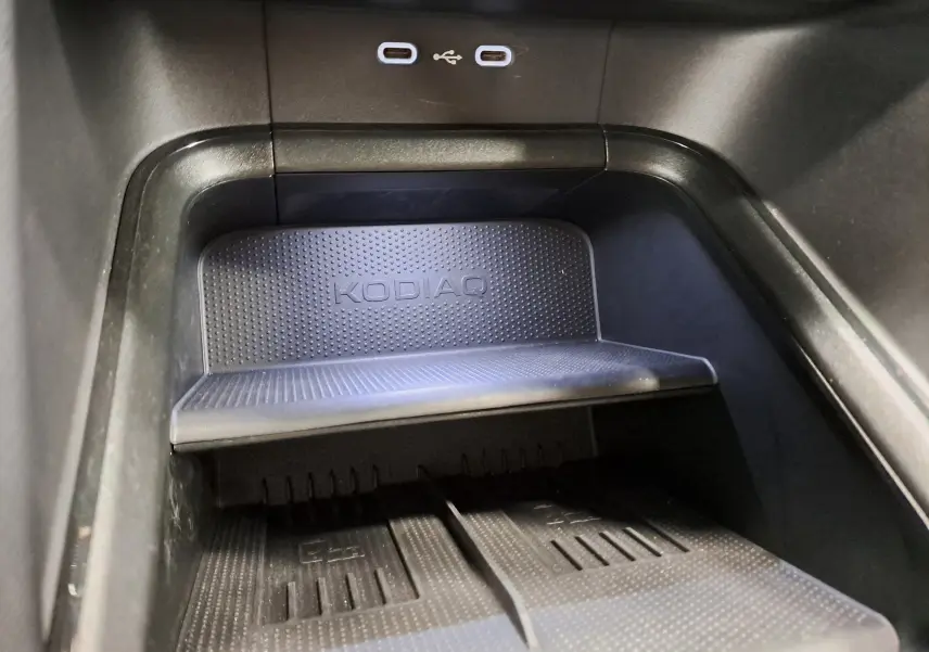 Gros plan sur la zone de recharge sans fil avec logo KODIAQ et deux ports USB-C dans un Skoda Kodiaq gris perle.