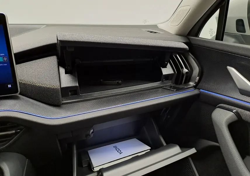Intérieur du Skoda Kodiaq 2025 gris perle, vue du tableau de bord côté passager avec boîtes à gants ouvertes et éclairage d’ambiance bleu.