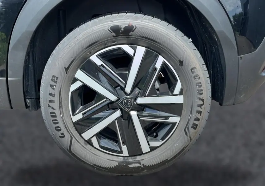 Gros plan sur la roue avant droite noire du Peugeot 2008 1.2 hybrid 145 style e-dcs6 avec jante à motifs géométriques.