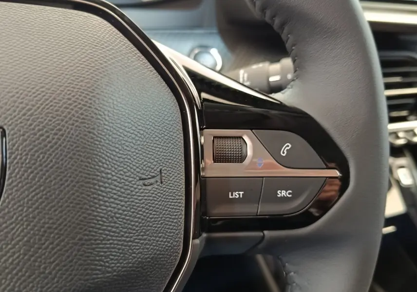 Gros plan sur la partie droite du volant cuir noir du Peugeot 208 électrique 2024 avec commandes audio intégrées.