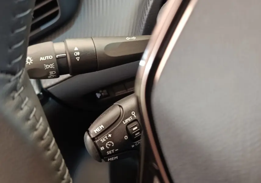 Gros plan sur les commandes au volant cuir noir de la Peugeot 208 électrique blanche, avec régulateur de vitesse.