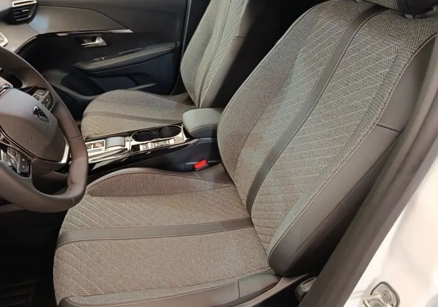 Intérieur de la Peugeot 208 électrique 2024, vue côté conducteur sur sièges tissu gris et console centrale noire brillante.
