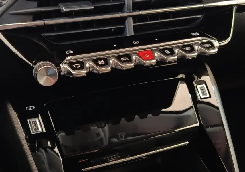 Vue rapprochée de la console centrale noire brillante avec boutons chrome et touches de commande sur Peugeot 208 électrique blanche.