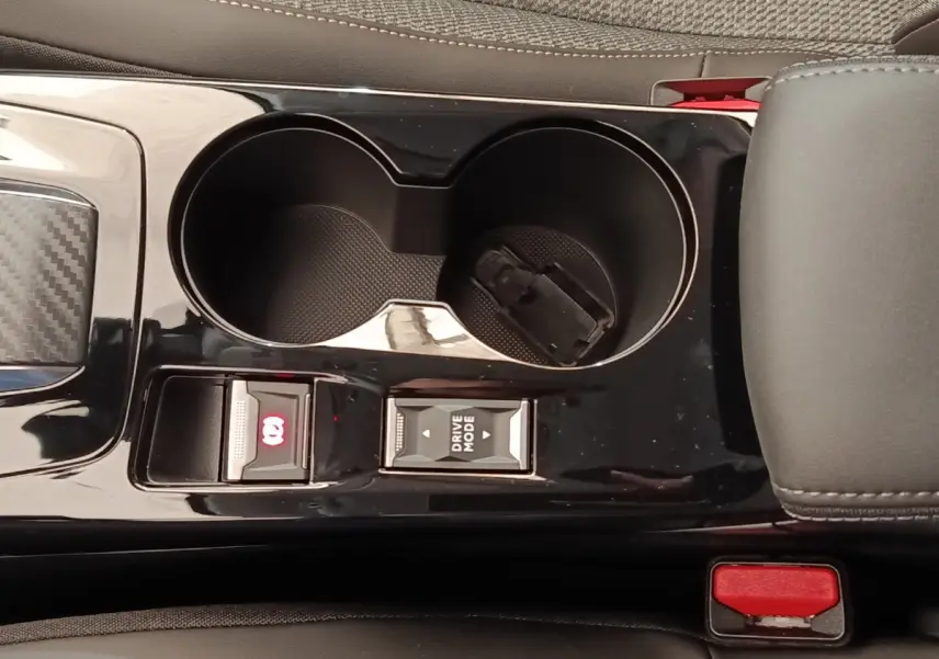Gros plan sur la console centrale noire brillante de la Peugeot 208 électrique 2024, avec commandes frein à main et mode de conduite.
