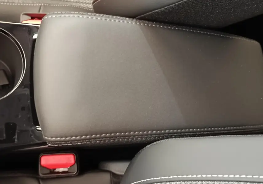 Détail de l'accoudoir central en cuir noir avec surpiqûres blanches dans l'habitacle d'une Peugeot 208 électrique.