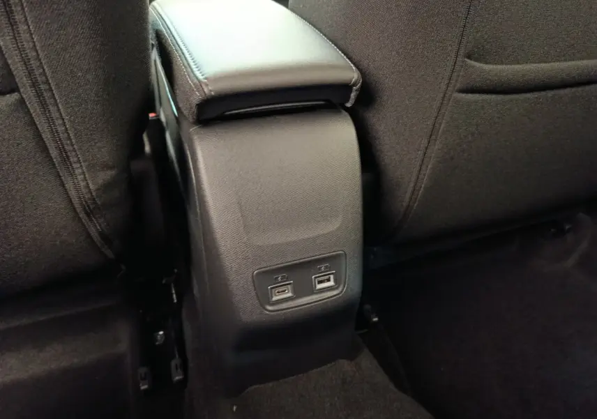 Vue rapprochée de la console centrale arrière noire avec ports USB dans une Peugeot 208 électrique blanche 2024.