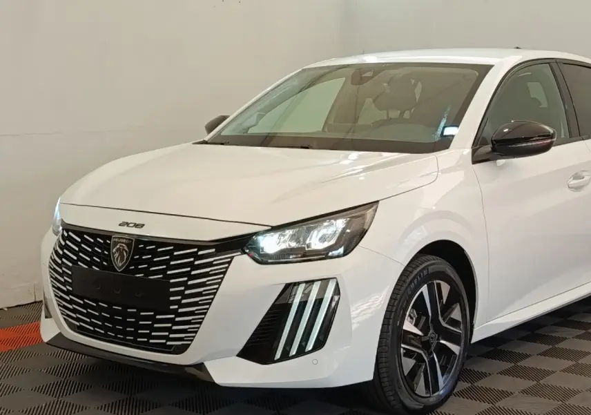 Peugeot 208 électrique blanche vue 3/4 avant droit, avec calandre noire distinctive et phares LED allumés.