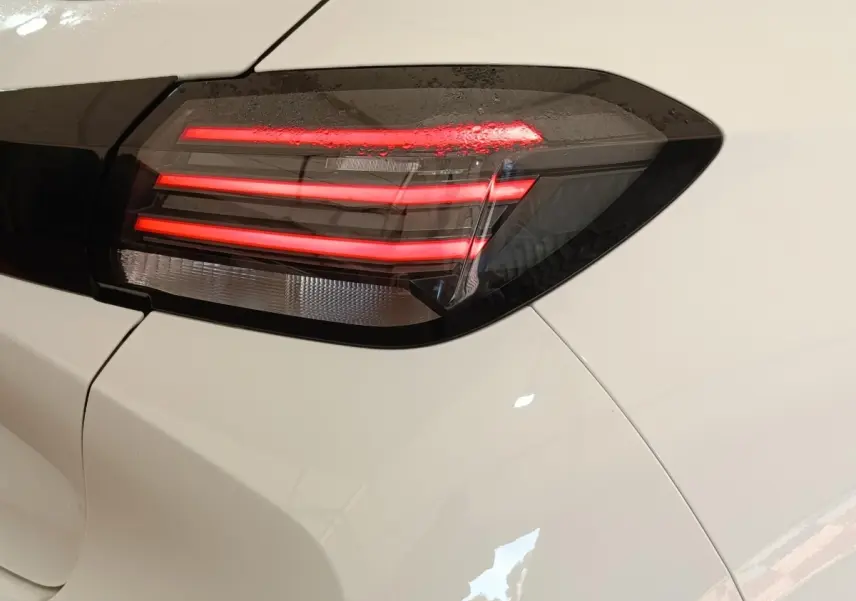 Gros plan sur le feu arrière droit rouge et noir d'une Peugeot 208 électrique blanche 2024.