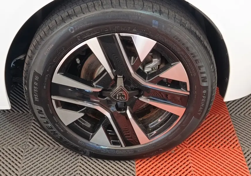 Gros plan sur la roue avant droite de la Peugeot 208 électrique blanche, jante alliage noir et argentée design moderne.