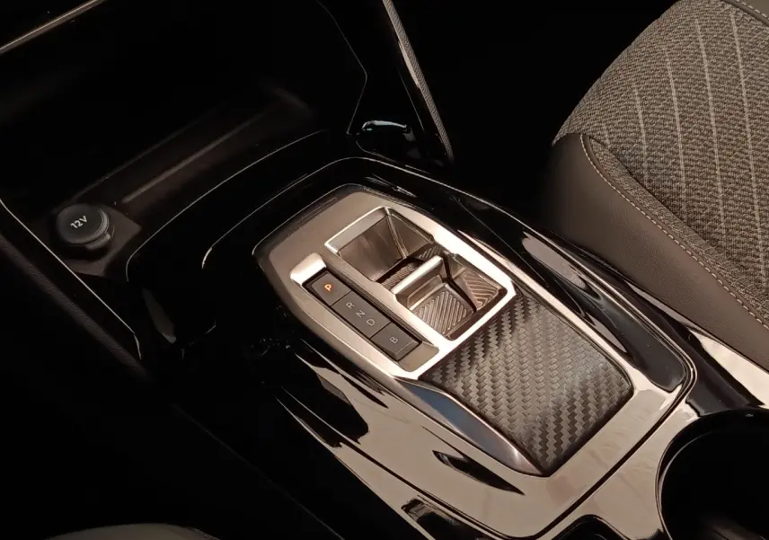 Gros plan sur la console centrale noire brillante avec sélecteur de vitesses et accoudoir tissu gris de la Peugeot 208 électrique.