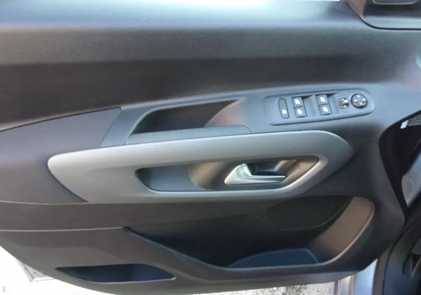 Vue intérieure du panneau de porte côté gauche du Citroën Berlingo gris Artense avec commandes de vitres et rétroviseurs.
