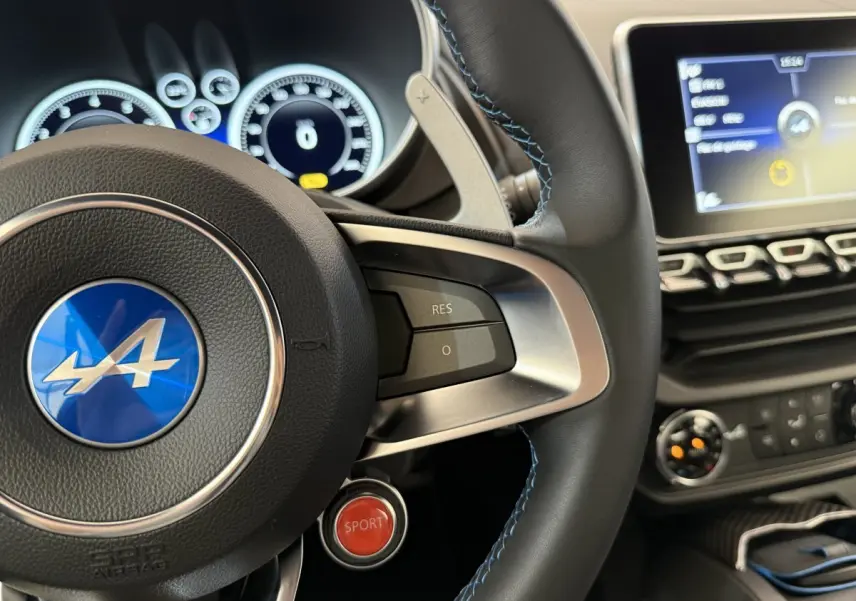 Gros plan sur le volant cuir de l'Alpine A110 Légende 2019 avec bouton rouge Sport et tableau de bord numérique.