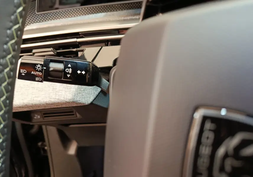 Détail du commodo d'éclairage à gauche du volant gris dans l'habitacle du Peugeot 3008 blanc 2025.