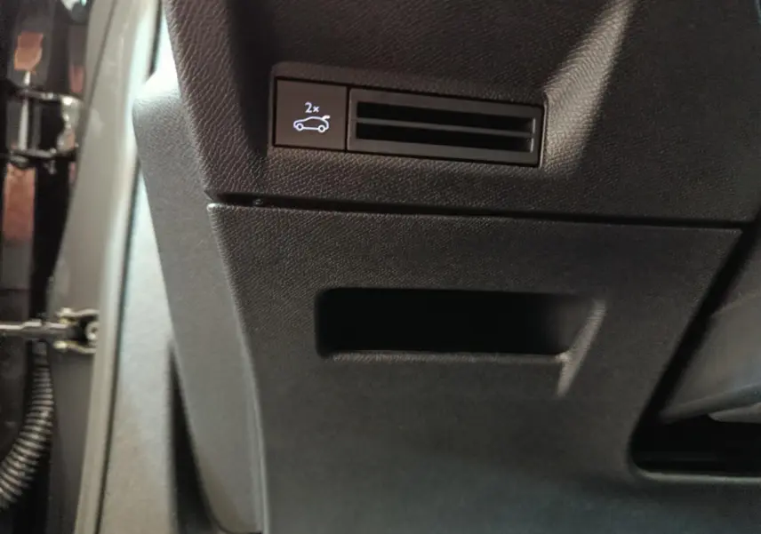 Détail intérieur montrant un bouton d'ouverture électrique du coffre sur la console côté conducteur du Peugeot 3008 blanc.