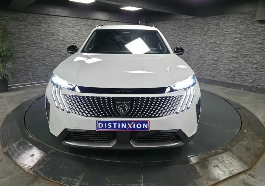 Vue avant d'un Peugeot 5008 blanc 2025 avec calandre noire laquée et feux LED distinctifs allumés.