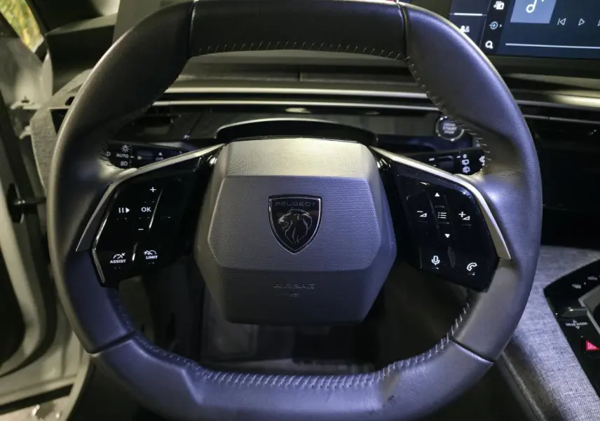 Volant compact noir avec logo Peugeot, commandes tactiles intégrées, vue frontale de l'habitacle du 5008 hybride blanc.