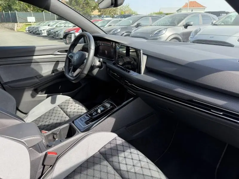 Vue intérieure côté conducteur de la Volkswagen Golf 1.5 eTSI R-Line 2024 avec sièges tissu à motif et tableau de bord moderne.