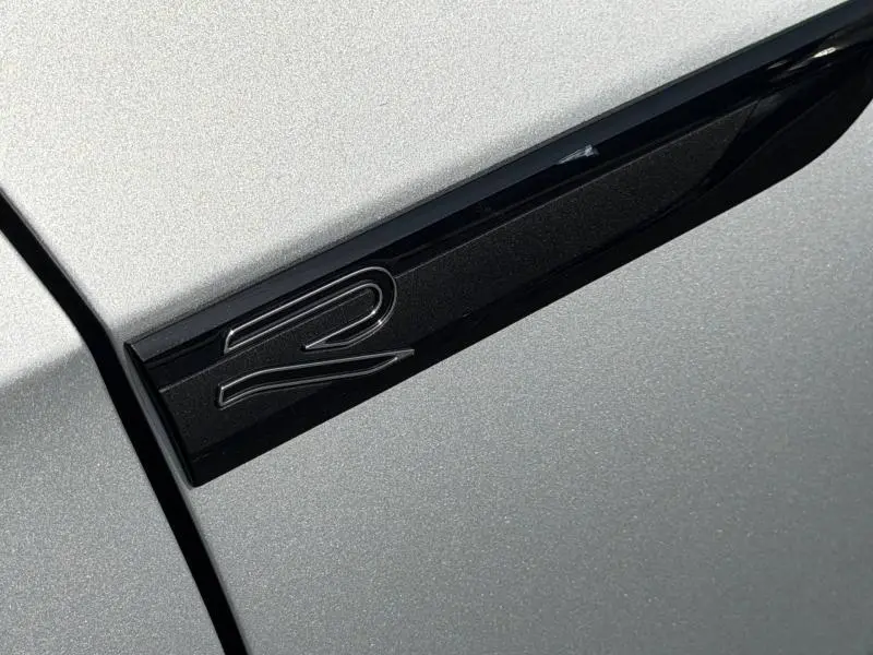 Détail de l'emblème R noir brillant sur la carrosserie Reflet d'Argent métallisée d'une Volkswagen Golf 2024.