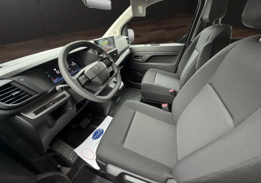 Vue intérieure côté conducteur du Citroën Jumpy gris foncé, avec tableau de bord moderne et sièges tissu gris.