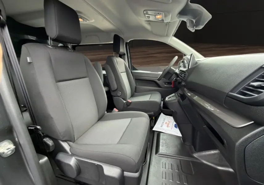 Vue intérieure côté droit du Citroën Jumpy gris foncé, montrant les sièges avant et le tableau de bord moderne.