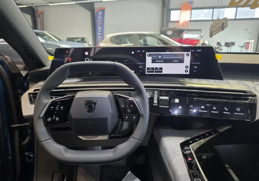 Vue intérieure centrée sur le volant compact et l'écran panoramique du tableau de bord du Peugeot 3008 hybride 2026.