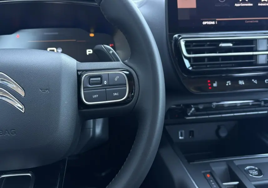 Gros plan sur le volant et la console centrale noire du Citroën C5 Aircross Hybrid 2025 avec commandes intégrées et écran tactile.