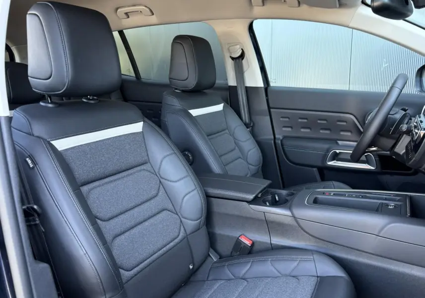 Vue intérieure côté conducteur du Citroën C5 Aircross Hybrid 2025, sièges cuir et tissu gris foncé avec console centrale.