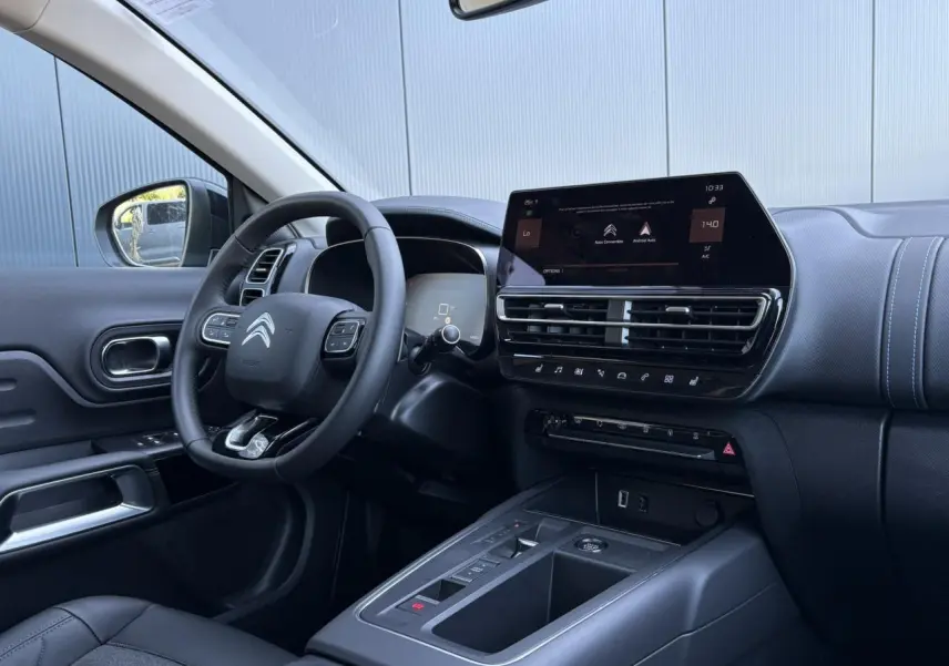 Intérieur du Citroën C5 Aircross Hybrid 2025, vue côté conducteur, tableau de bord noir avec écran tactile et volant cuir.