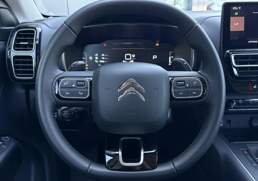 Vue centrée sur le volant noir du Citroën C5 Aircross Hybrid 2025 avec commandes intégrées et tableau de bord numérique.