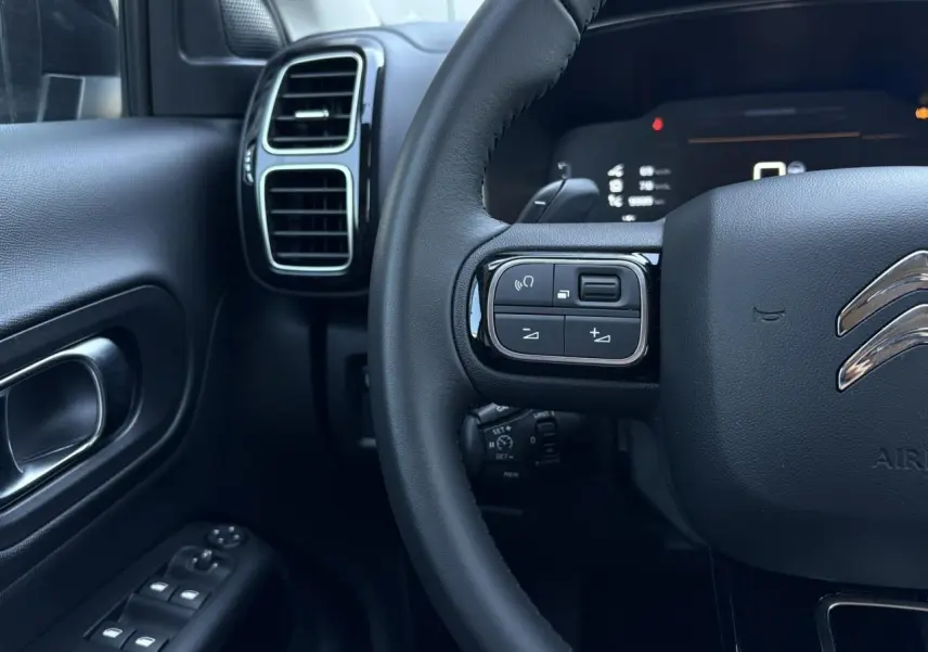 Vue rapprochée du volant et de la portière gauche du Citroën C5 Aircross Hybrid, intérieur noir avec commandes au volant.