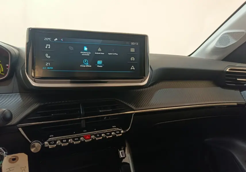 Vue intérieure du tableau de bord de la Peugeot 208 électrique 2024, écran tactile central et finition carbone gris.