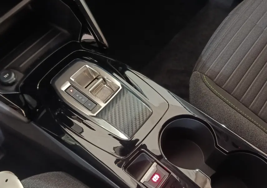 Gros plan sur la console centrale noire brillante avec levier de boîte automatique et frein à main électrique, siège tissu gris à surpiqûres vertes.