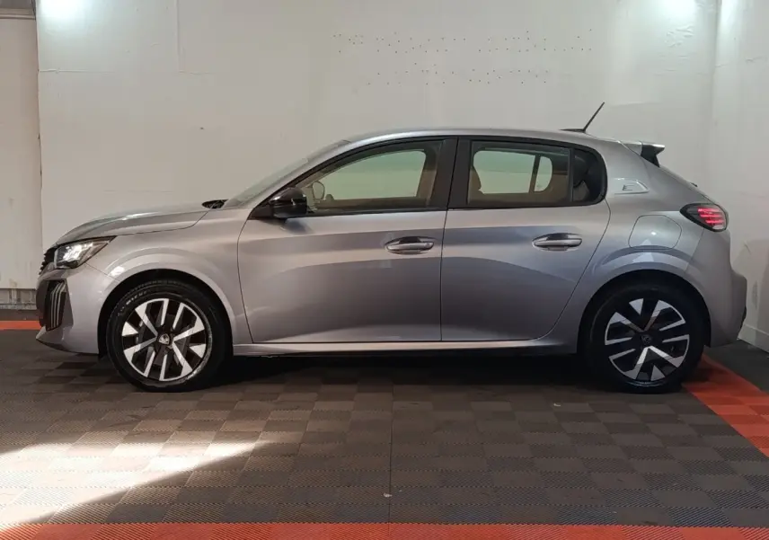 Peugeot 208 électrique gris clair vue de profil côté gauche dans un garage avec sol noir et rouge.