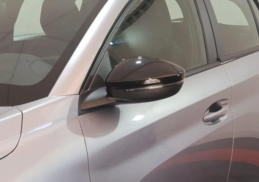 Vue rapprochée du côté gauche d'une Peugeot 208 électrique gris clair avec rétroviseur noir brillant.