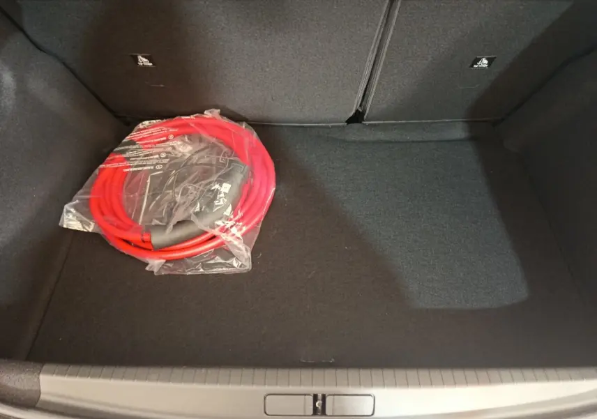 Coffre ouvert de Peugeot 208 électrique gris clair vu de dessus, avec câble de charge rouge emballé posé à gauche.
