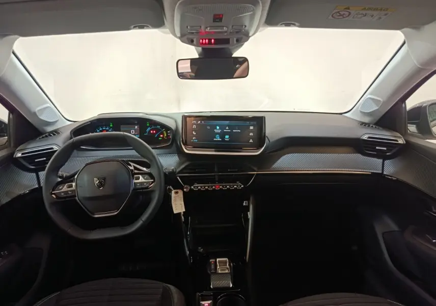 Vue intérieure avant de la Peugeot 208 électrique 2024, tableau de bord noir avec écran tactile central et volant cuir multifonctions.