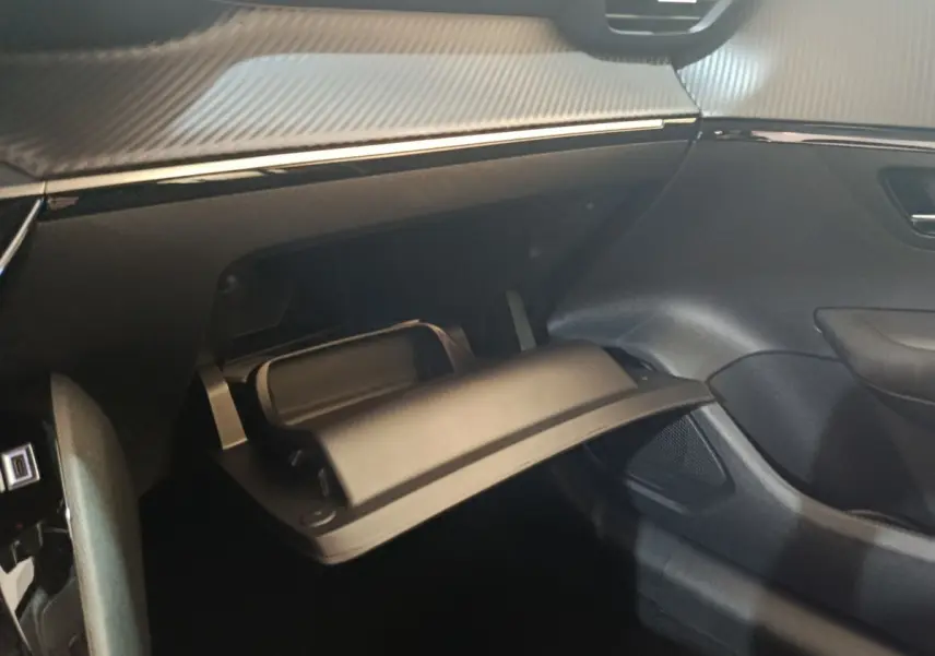 Intérieur de la Peugeot 208 électrique 2024, vue sur la boîte à gants ouverte côté passager avec finition noire et détails carbone.