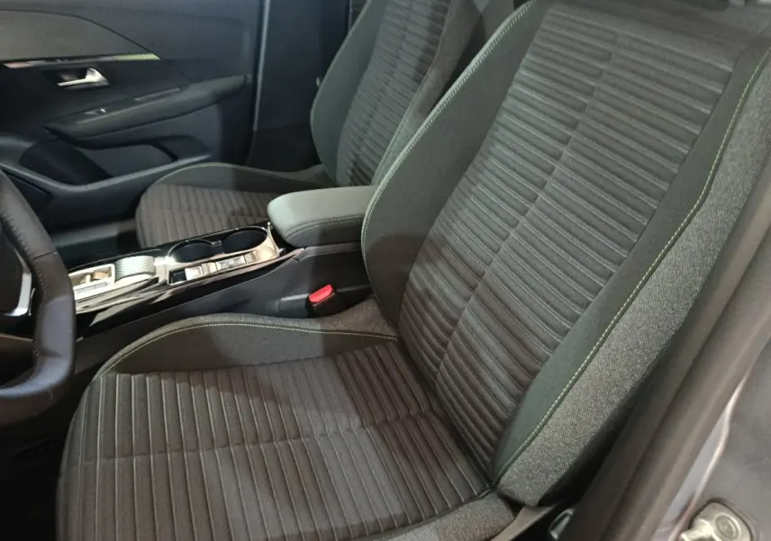 Vue intérieure côté conducteur de la Peugeot 208 électrique 2024, sièges tissu gris avec surpiqûres vertes et console centrale.