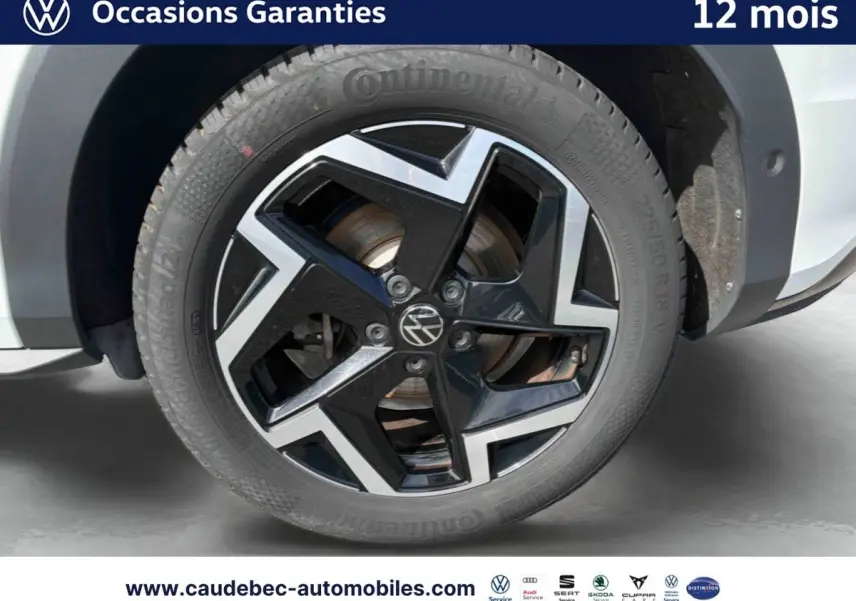 Gros plan sur la jante avant droite noire et argentée du Volkswagen T-Roc blanc, avec logo VW central visible.