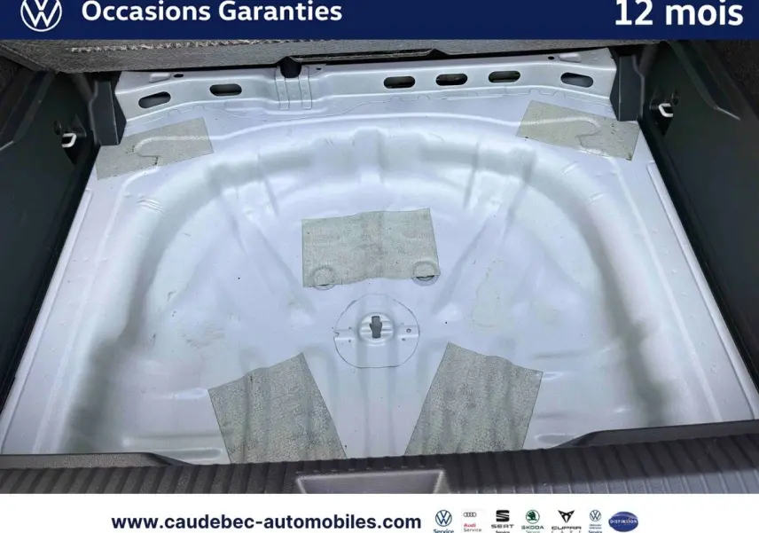 Coffre ouvert d’un Volkswagen T-Roc blanc, vue plongeante sur l’espace de rangement sans roue de secours.