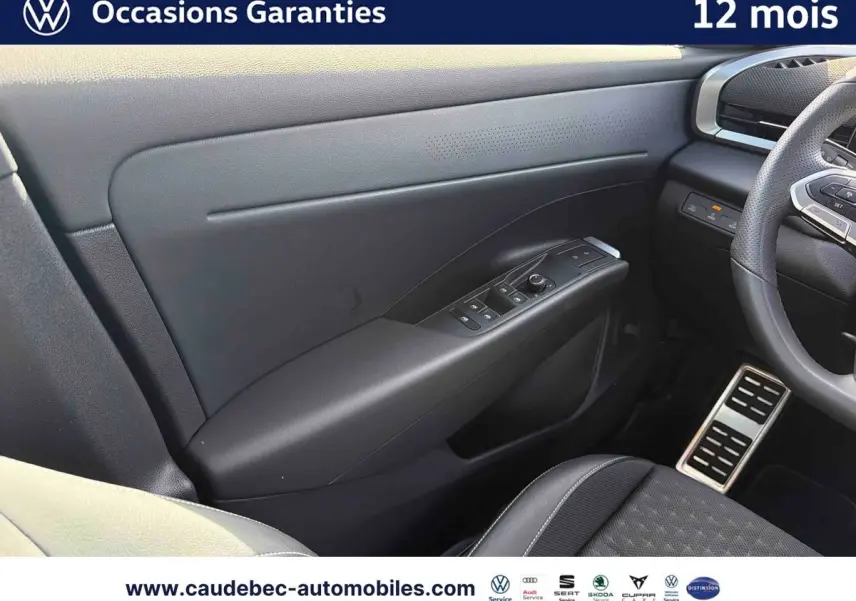 Vue intérieure côté conducteur du Volkswagen T-Roc blanc, mettant en valeur la porte avec commandes électriques et volant multifonction.