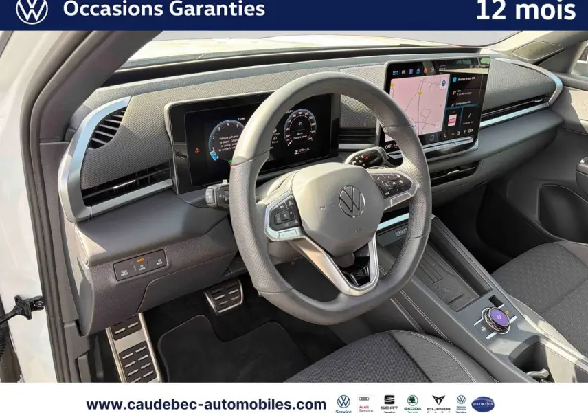 Vue intérieure côté conducteur du Volkswagen T-Roc blanc 2025, volant multifonction cuir et écran tactile central visible.