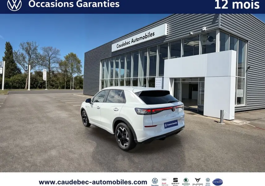 Volkswagen T-Roc blanc en 3/4 arrière droit, avec feux LED et jantes noires brillantes, devant un bâtiment moderne.